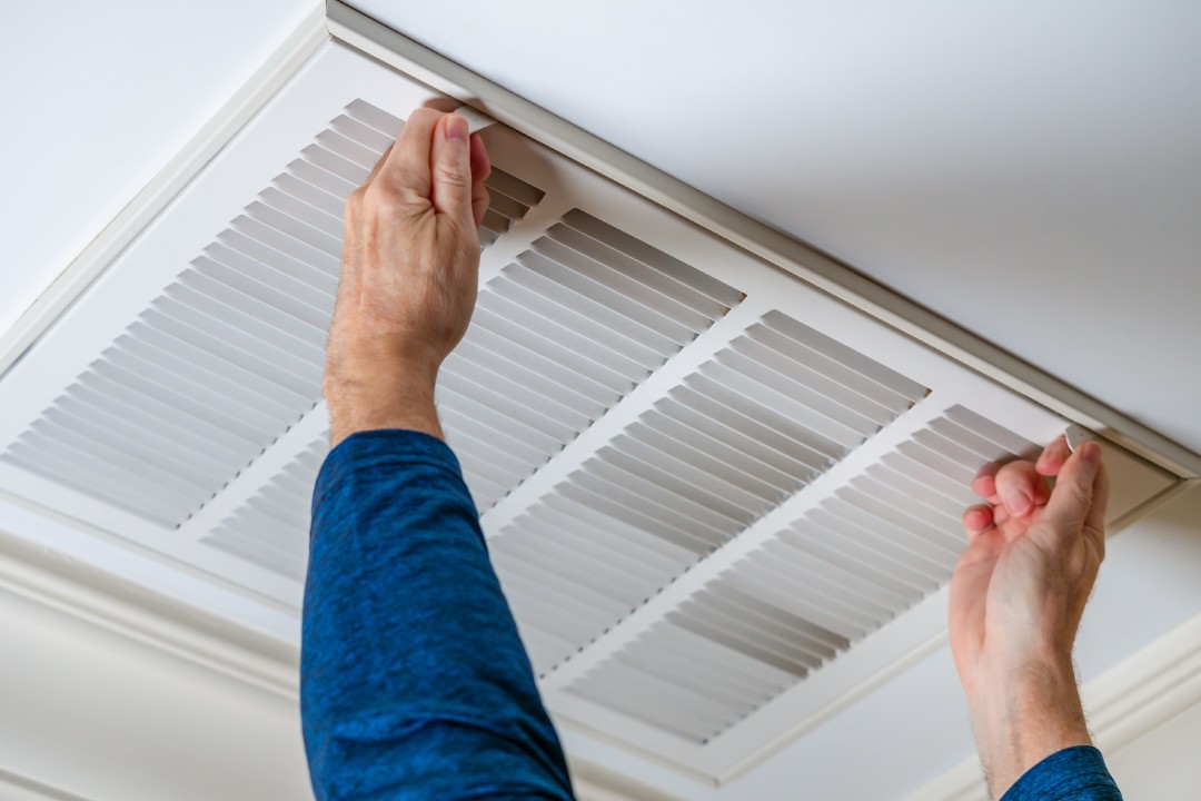 Man opening ceiling air vent to replace dirty HVAC air filter. Home air duct system maintenance for clean air